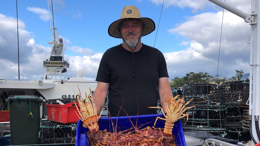 man on boat holding up lobsters
