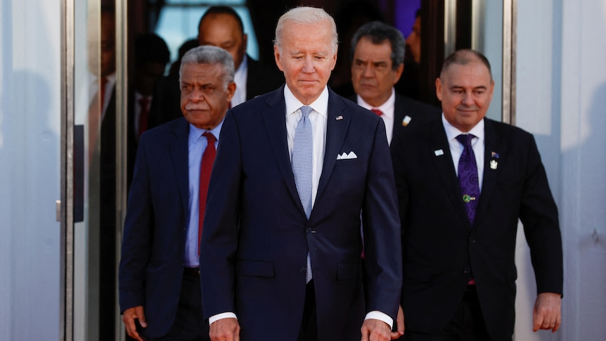 Joe Biden walks out of a doorway at the White House with Pacific Island leaders behind him