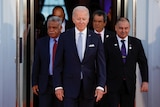 Joe Biden walks out of a doorway at the White House with Pacific Island leaders behind him