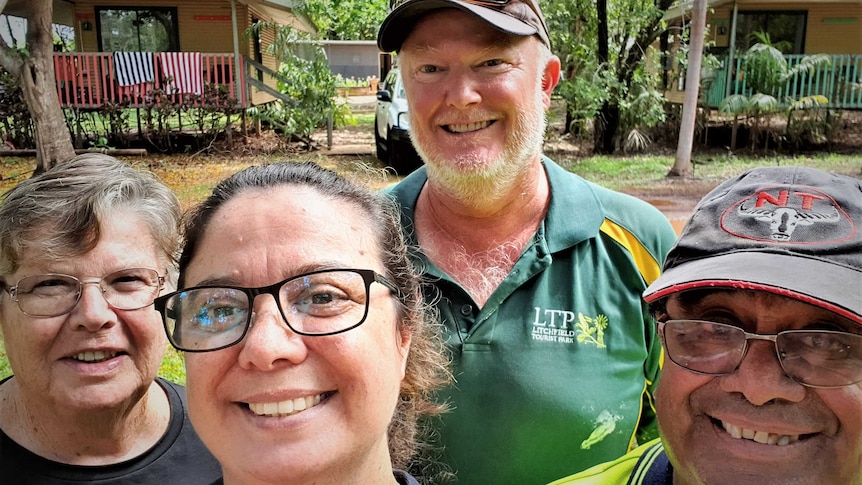 Four people in a selfie smiling in a bush setting with a holiday chalet behind them.