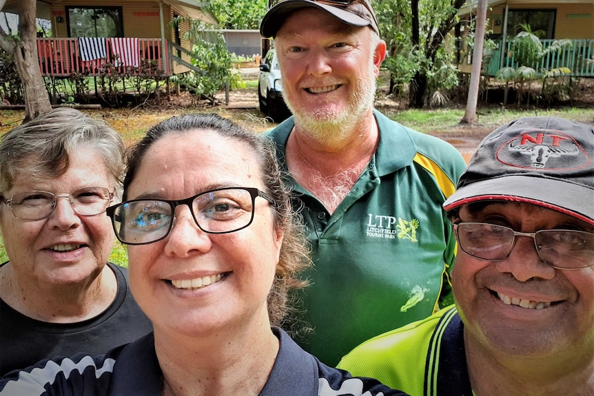 Four people in a selfie smiling in a bush setting. Holiday chalet in background