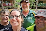 Four people in a selfie smiling in a bush setting with a holiday chalet behind them.