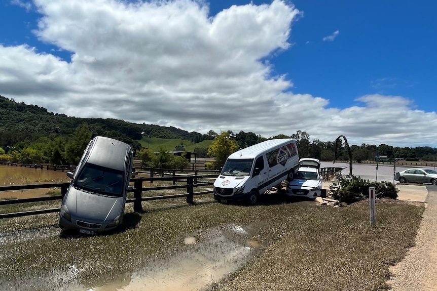 Cars washed up against a fence in a water-logged area.