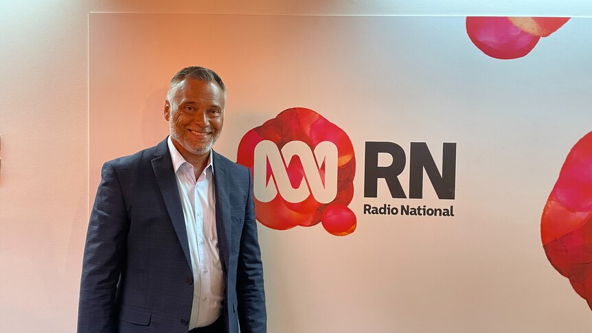 ABC Host Stan Grant smiles in a suit in front of an RN Background