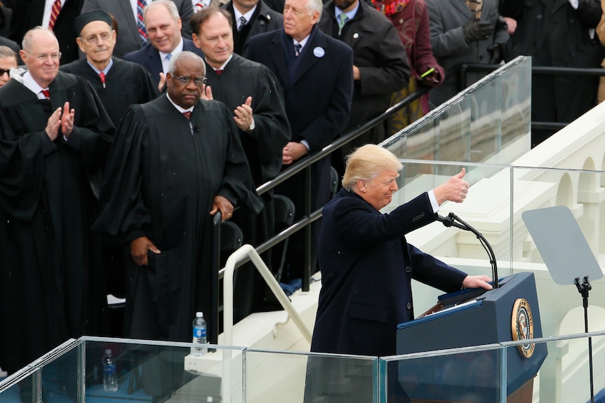 Donald Trump gives a thumbs up while several members of the US Supreme Court watch on