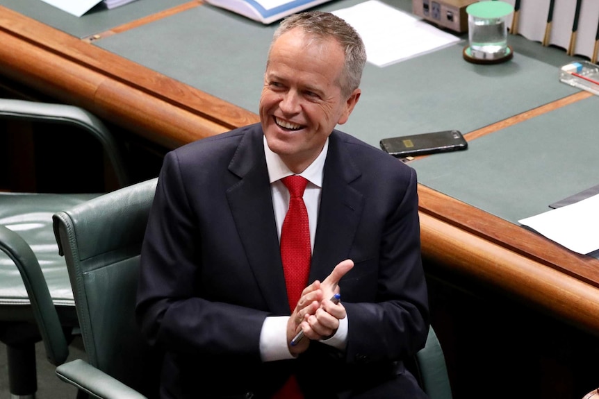 Bill Shorten looks into the distance and smiles while sitting in the Opposition leader's seat in Parliament House