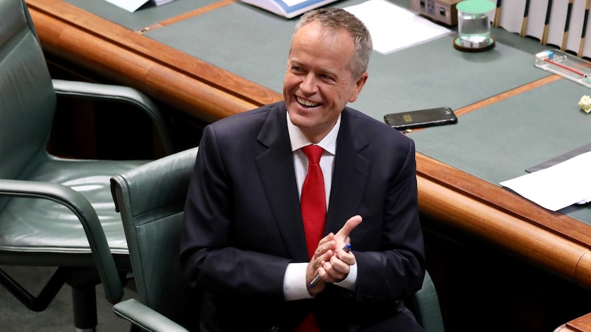 Bill Shorten looks into the distance and smiles while sitting in the Opposition leader's seat in Parliament House
