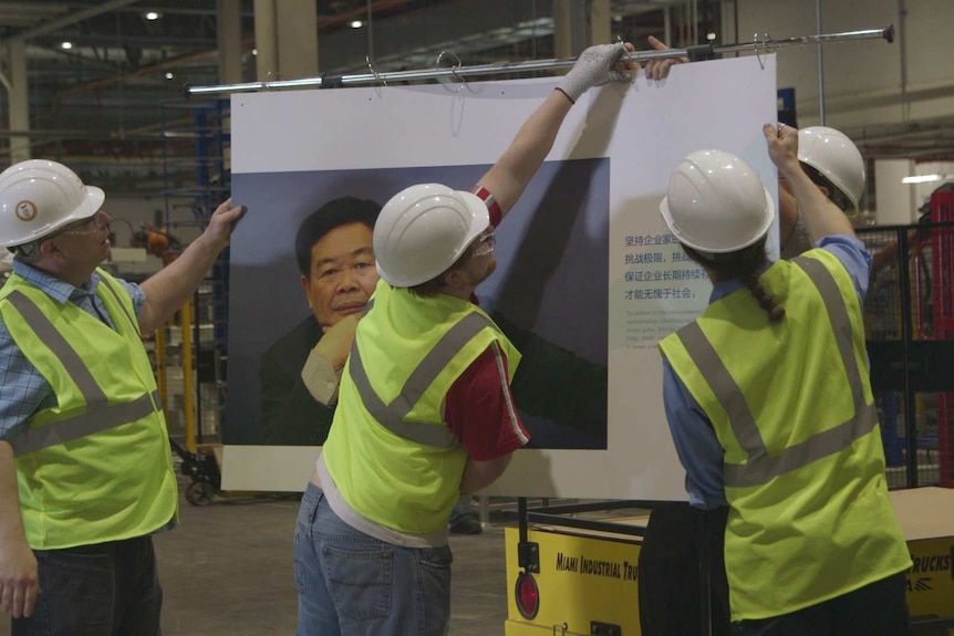 Workers hang up a poster of the boss of their factory, Chairman Cao