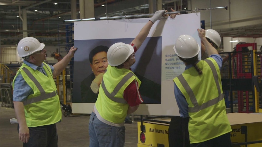 Workers hang up a poster of the boss of their factory, Chairman Cao