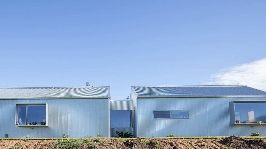 A landscape photo shows a metal-clad single-storey contemporary home sitting on a gentle hill.