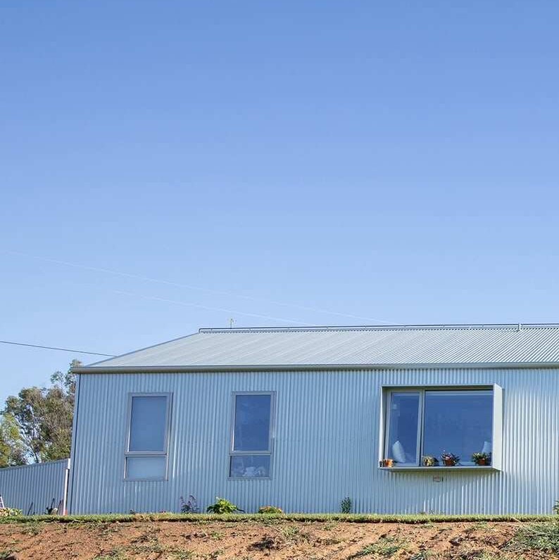 A landscape photo shows a metal-clad single-storey contemporary home sitting on a gentle hill.
