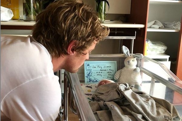 Rory Sloane sits down leaning over looking at his baby
