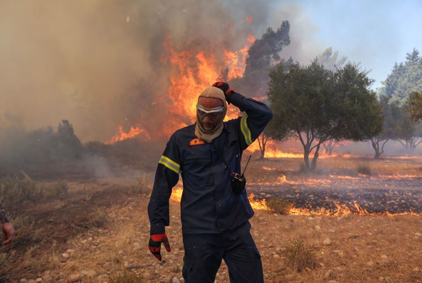 A firefighter walks next to rising flames as a wildfire burns near the village of Vati