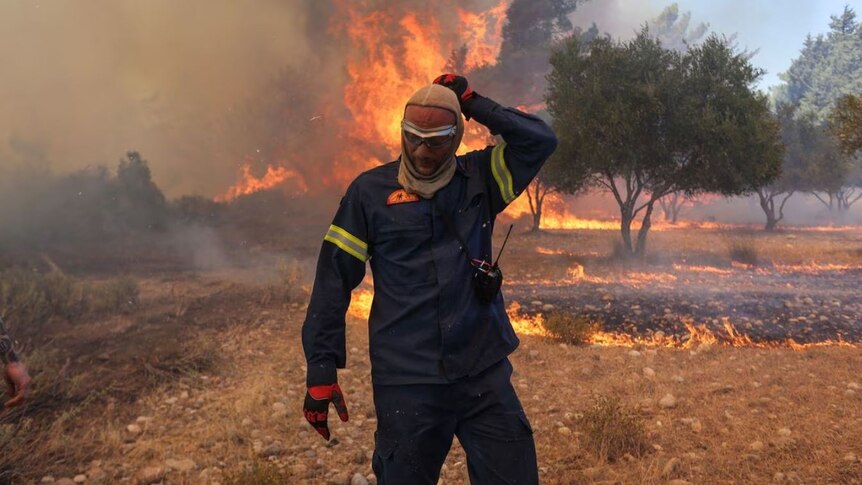 A firefighter walks next to rising flames as a wildfire burns near the village of Vati