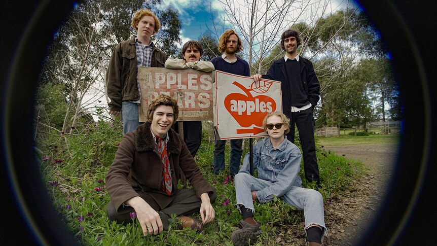 Six members of Bones and Jones stand around signs advertising apples and pears