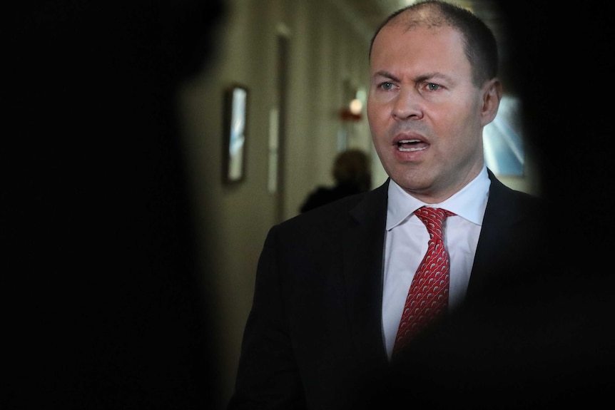 Josh Frydenberg wears an angry facial expression. He is surrounded by shadow.