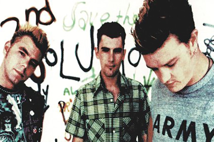 three members of The Living End pose in a white studio that has been covered in graffiti