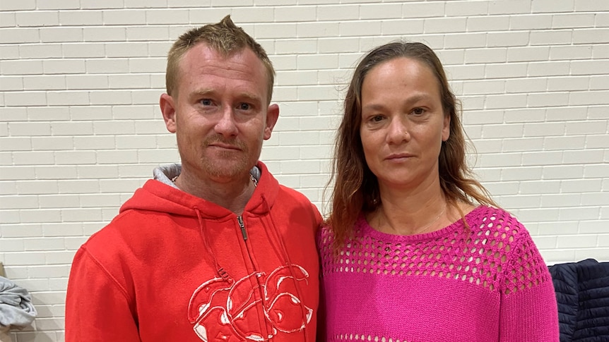 Man wearing a red hoodie standing next to a woman in a pink jumper. 
