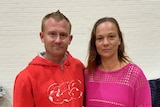 Man wearing a red hoodie standing next to a woman in a pink jumper. 