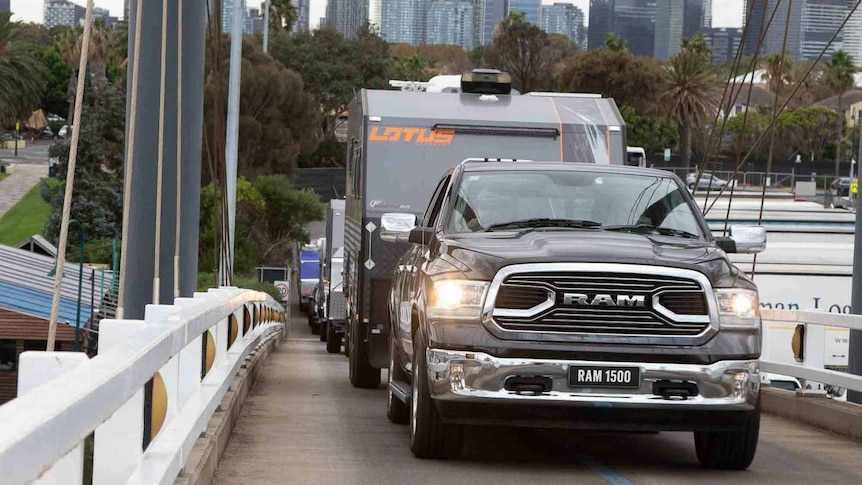 A massive pickup truck tows a caravan along a narrow bridge in an urban area.