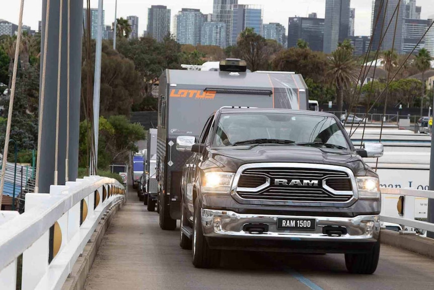 A massive pick up truck tows a caravan along a narrow bridge in an urban area.