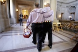 Two men holding hands with their backs to the camera walking away to get married.
