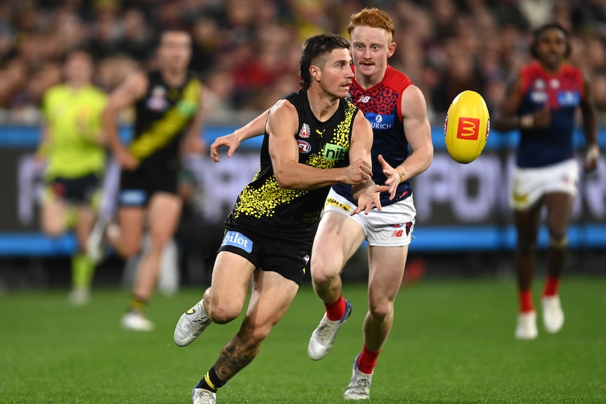 A Richmond player looks inboard and handballs while a Melbourne defender tries to close in.