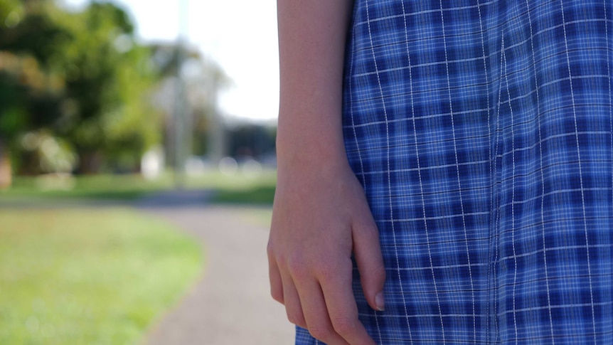Closeup of a girl's hand. The girl is wearing a blue-checkered school dress.