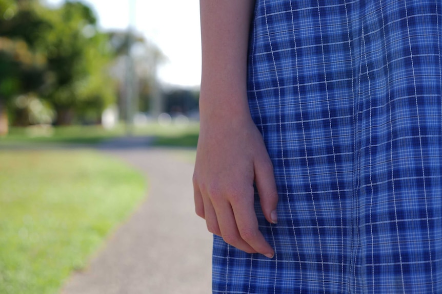 Closeup of a girl's hand. The girl is wearing a blue-checkered school dress.