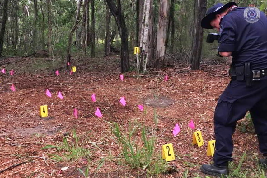 Police investigator takes photos at a rural property with police markers on the ground where a man was found dead.