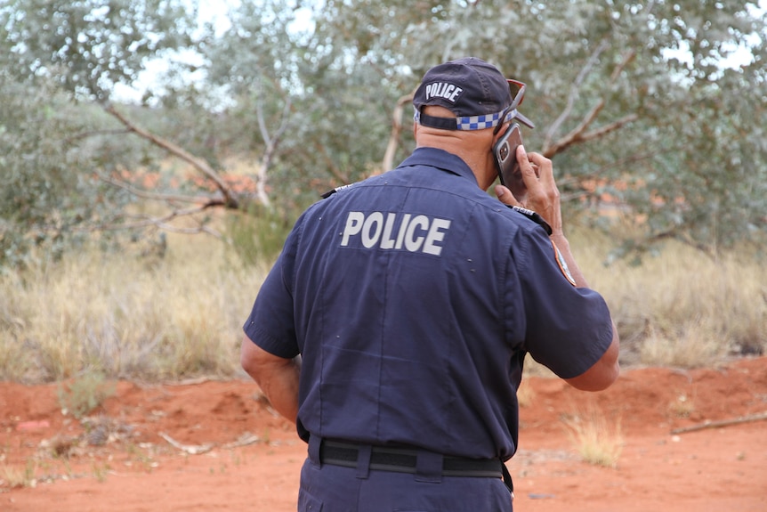 The back of a man in police unifiorm with red dirt in the background.