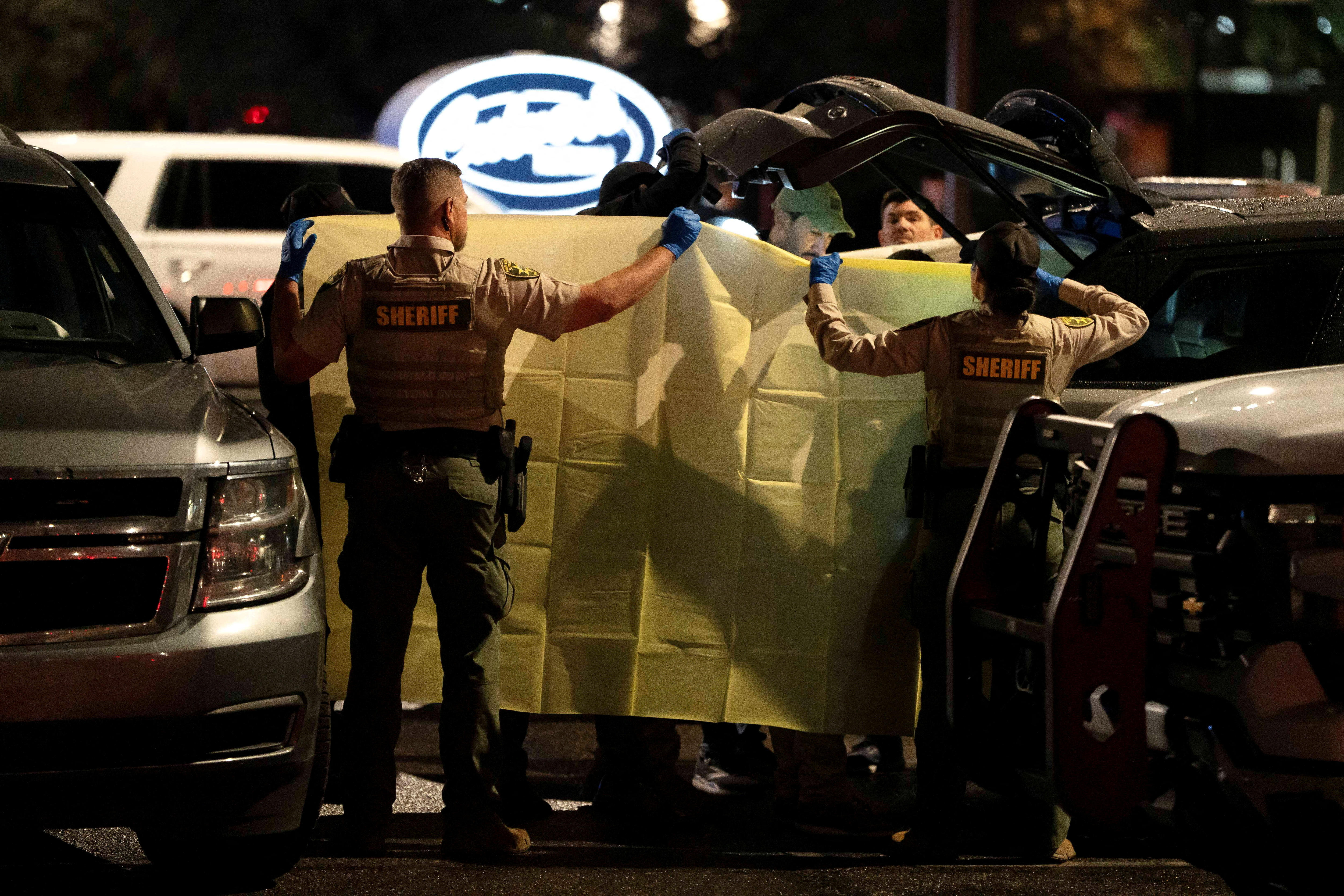 Sheriffs hold up a yellow sheet as other officers process evidence from the boot of a grey Range Rover at night in a car park