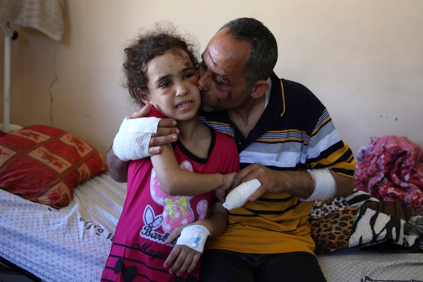 A man kisses a young girl on the cheek. Both have visable facial and arm injuries.