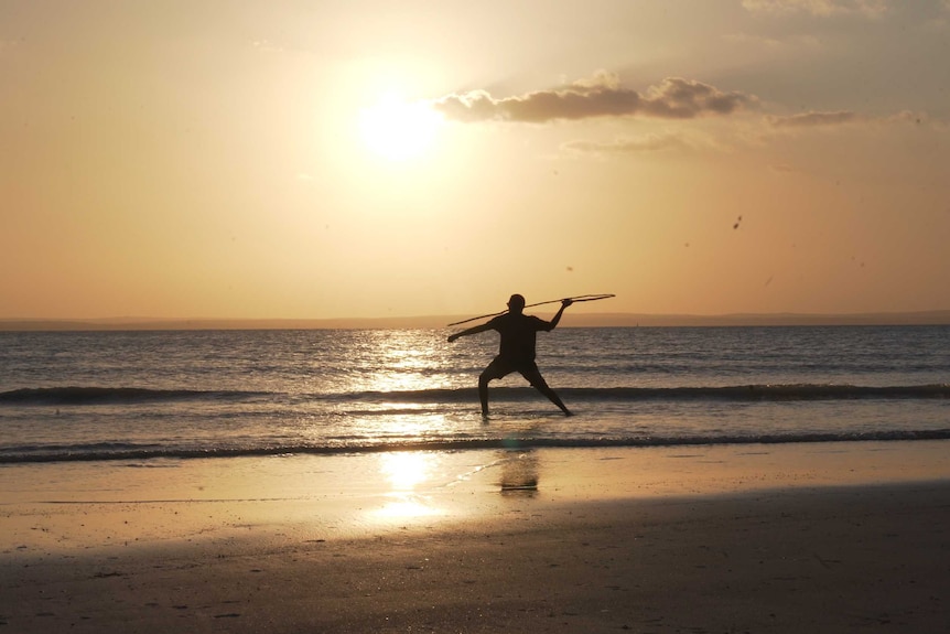 Sunset shot of man throwing spear on Arnhem Land beach.