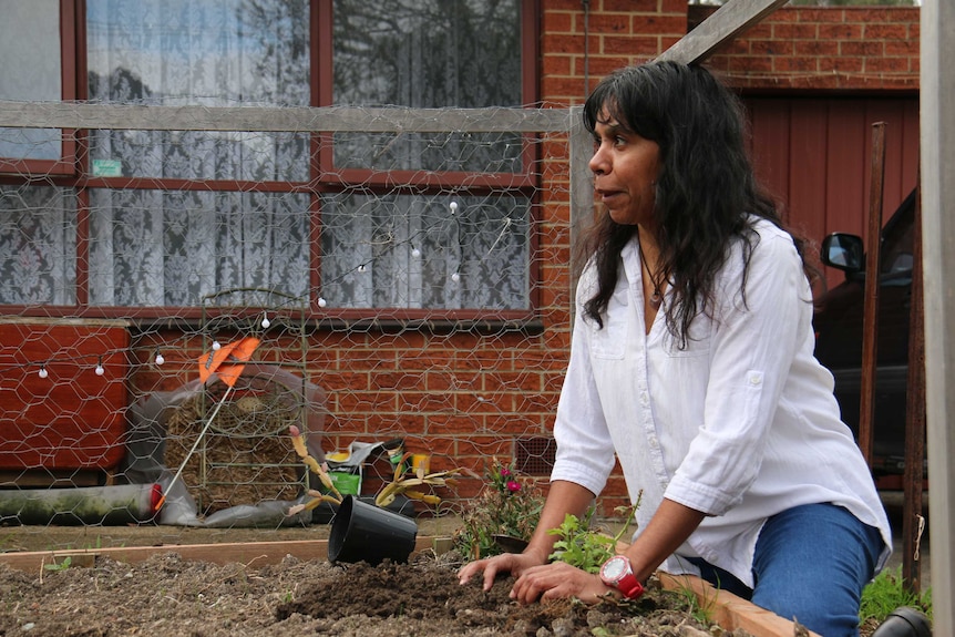 Sonya Singh kneels by a sandbox with her hands in the soil.