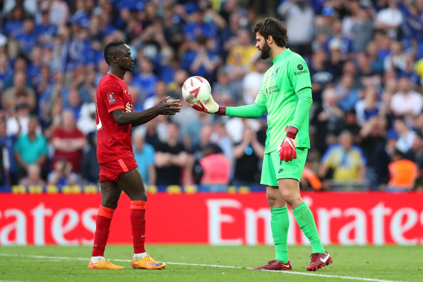 A goalkeeper wearing green gives a ball to a player wearing red during a game
