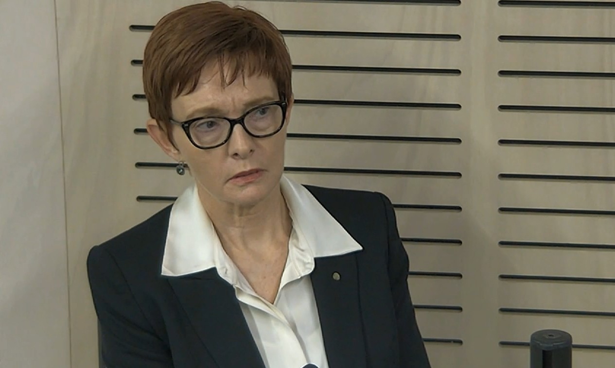 A woman with short red hair in a white dress shirt and blazer.