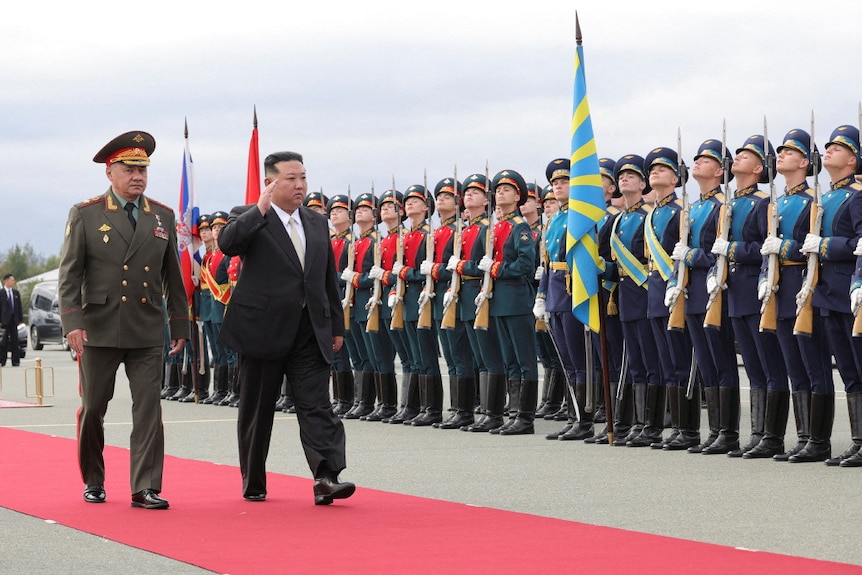 Two men walk down a red carpet past soldiers who stand to attention.