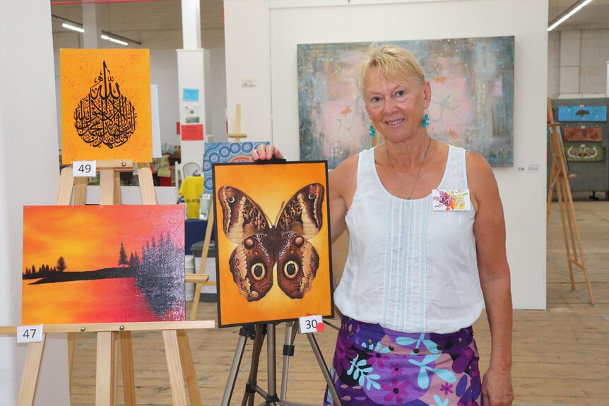 A woman stands next to some paintings on a stand