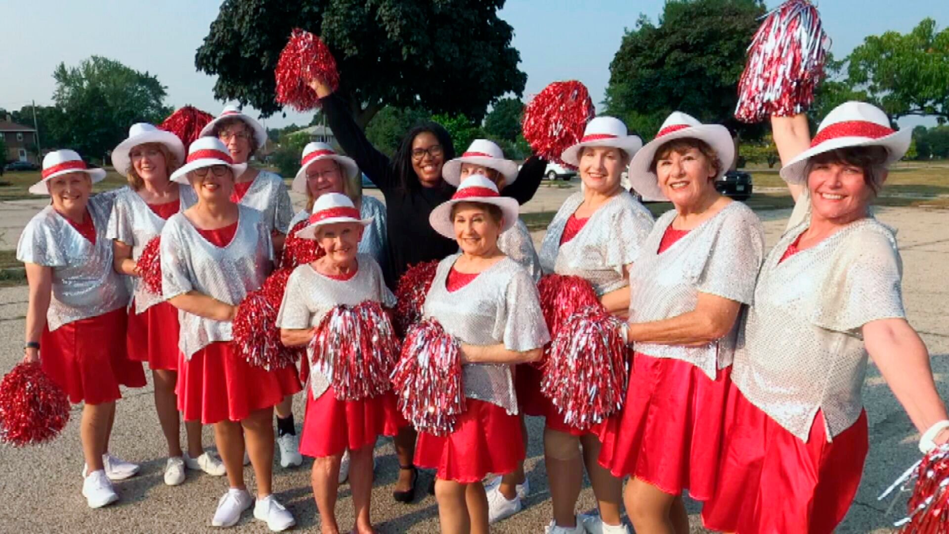 A group of mature aged women dresses in red with glittery shirts, matching hats and pom poms. 