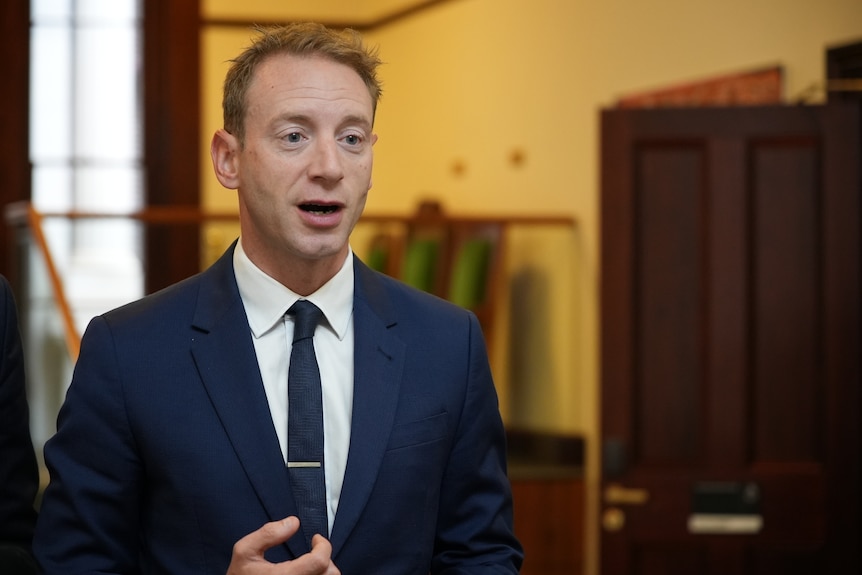 A man in a blue suit and tie and white shirt talking