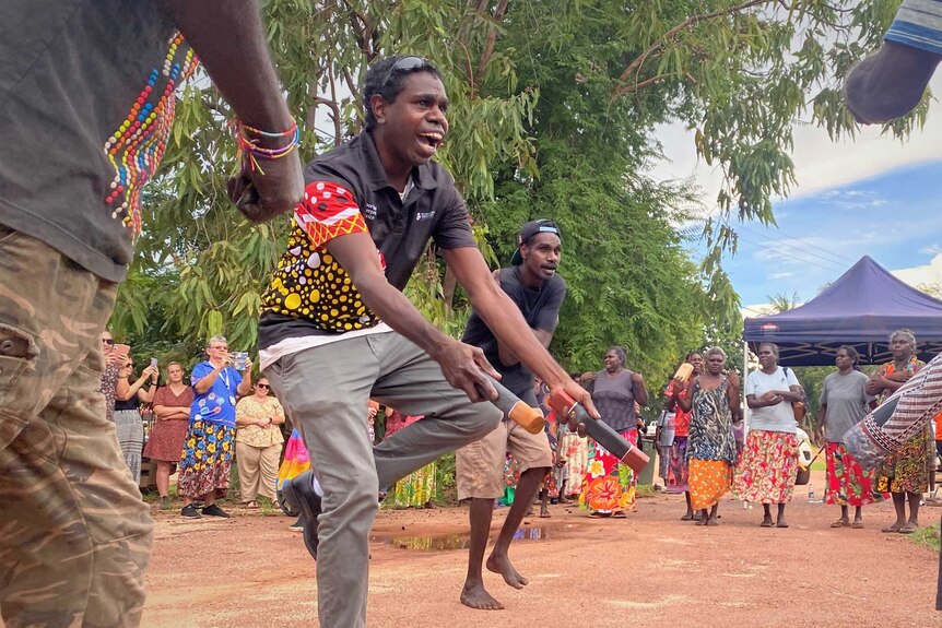 A group dances with one man clapping sticks at a ceremony at the Maningrida health clinic.