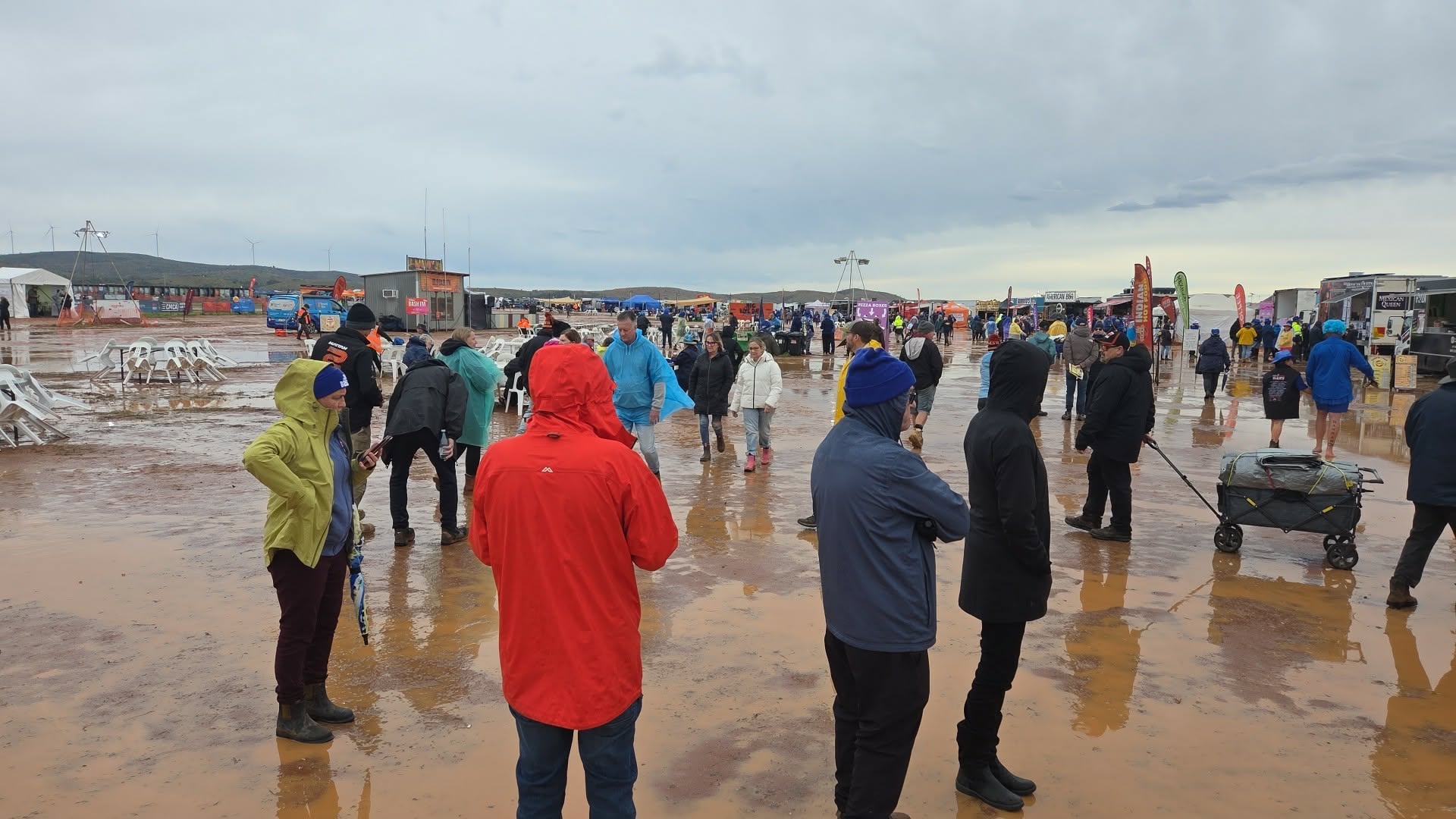 People walking around at festival site with muddy puddles and water wearing rain gear