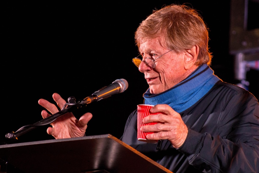 A man dressed warmly in June 2021 addressing a crowd in the dark
