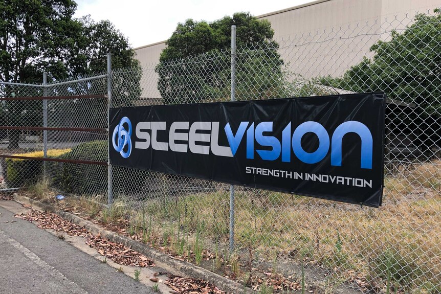 A black canvas sign with the words 'Steelvision' hangs on a tall metal fence