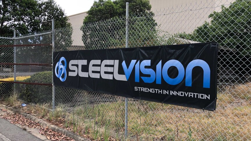 A black canvas sign with the words 'Steelvision' hangs on a tall metal fence