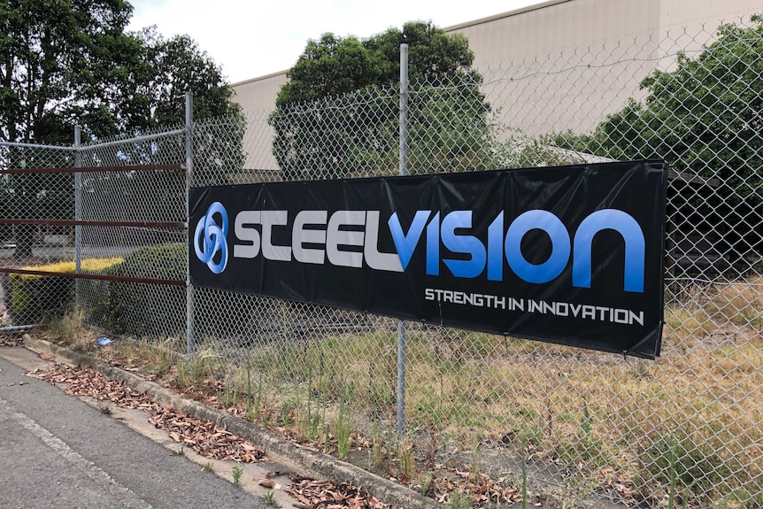 A black canvas sign with the words 'Steelvision' hangs on a tall metal fence