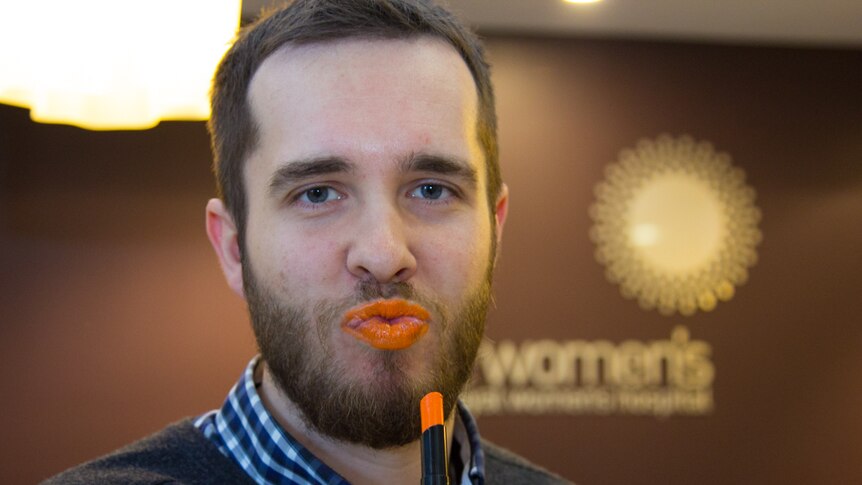 A bearded man wears orange lipstick.