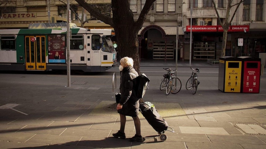 A woman wearing a face mask walks in Melbourne's CBD. A tram can be seen in the background.