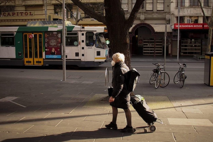 A woman wearing a face mask walks in Melbourne's CBD. A tram can be seen in the background.